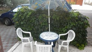 Une terrasse avec une table et deux chaises, un parasol et une voiture garée à proximité.