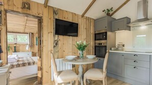 L’intérieur chaleureux d’un chalet, avec un revêtement mural en bois, un coin repas comprenant des chaises et une table, une cuisine équipée d’armoires et d’une cuisinière, et un téléviseur fixé au mur.