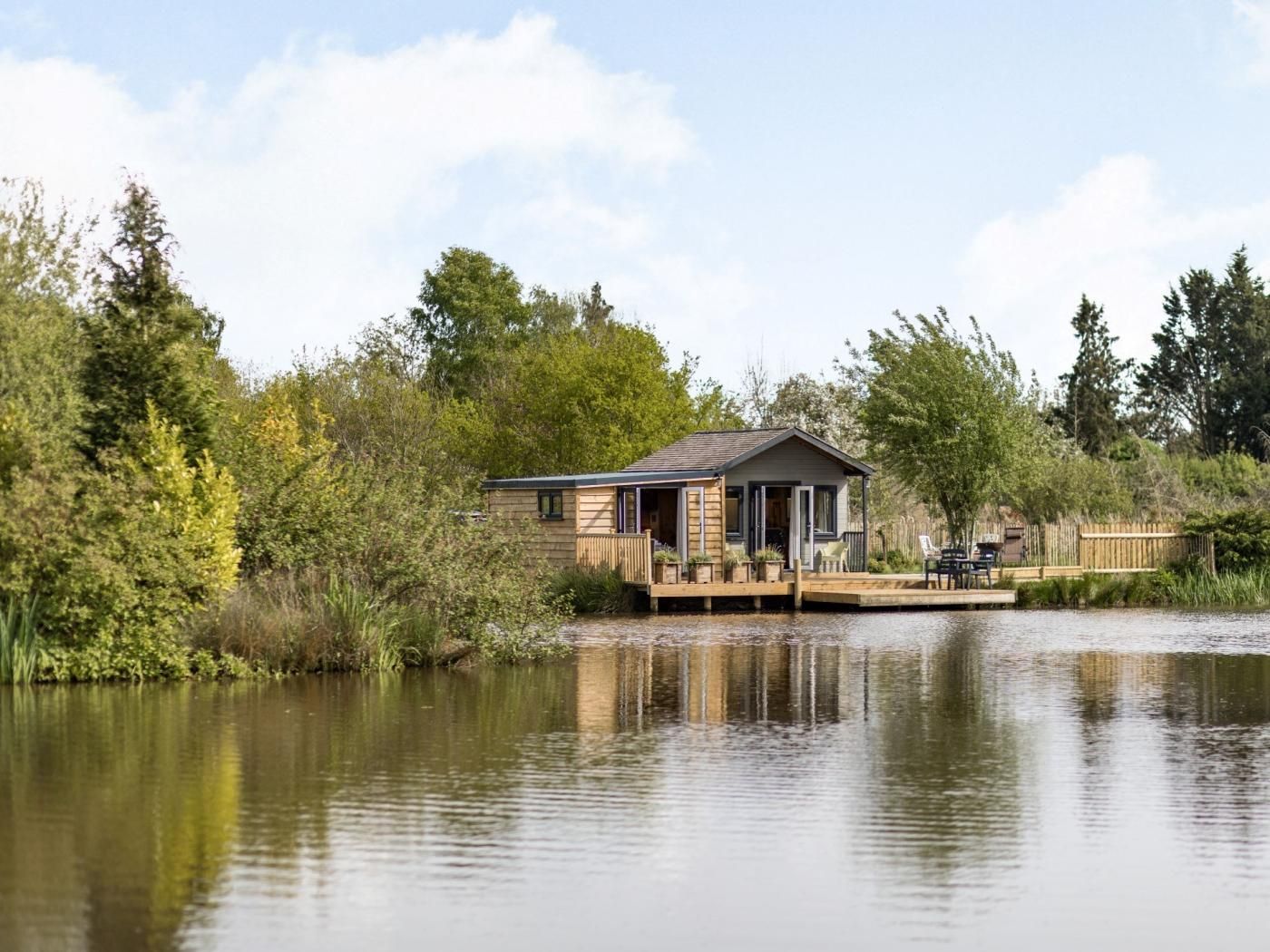 Un chalet au bord du lac, doté d’une terrasse et entouré d’arbres et de végétation.