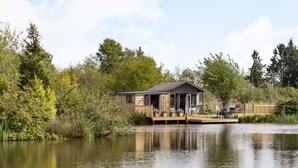 Un chalet au bord du lac, doté d’une terrasse et entouré d’arbres et de végétation.