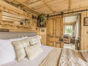 A rustic wooden room with a bed, a sofa, and a door leading to another room.