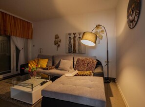 A living room with a sofa, a glass coffee table, a floor lamp, and wall art. - Classic One Bedroom Apartment with Terrace (Vukovar)