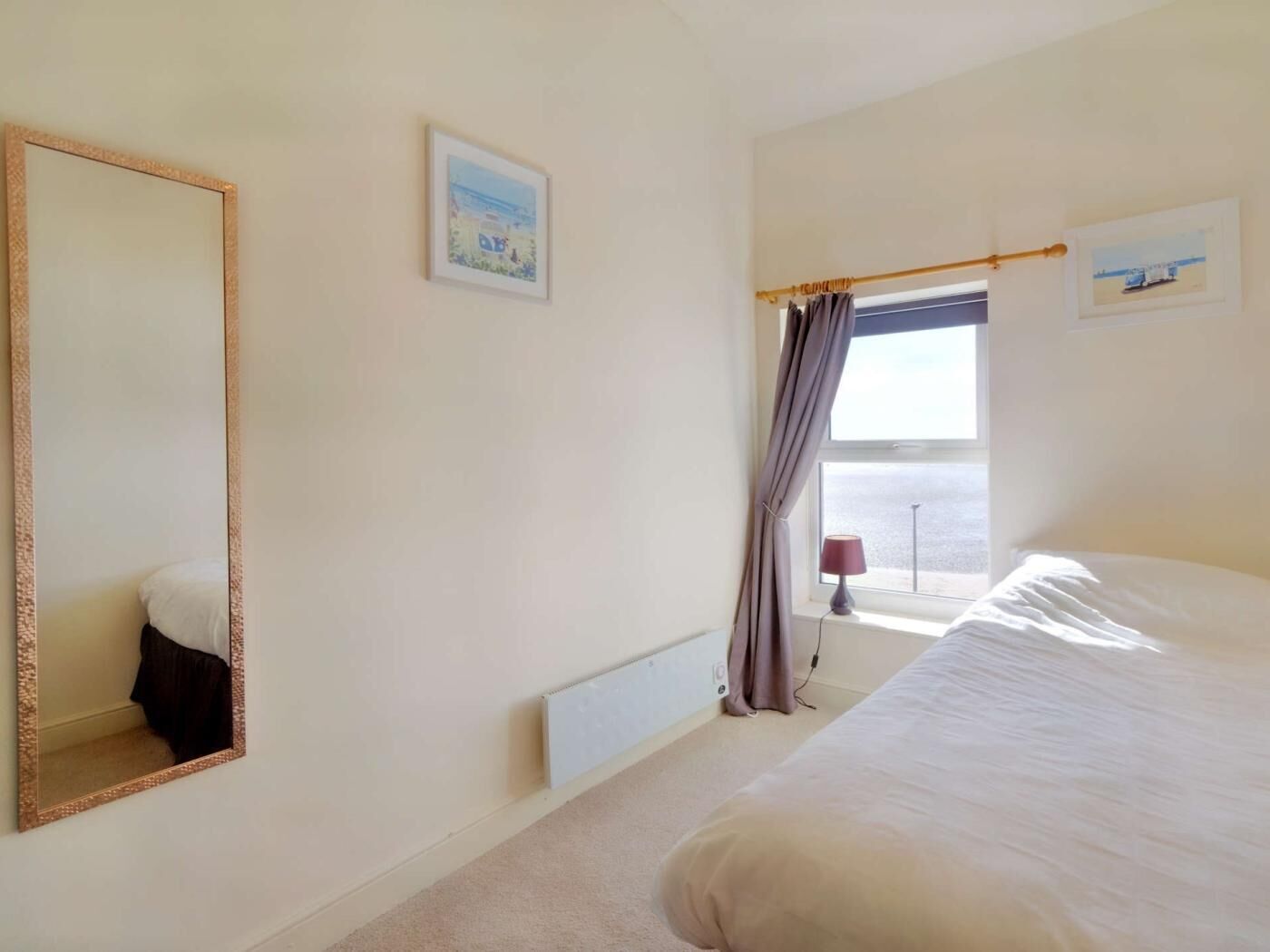 Une chambre à coucher avec un grand lit, un miroir, une fenêtre avec des rideaux et un radiateur.