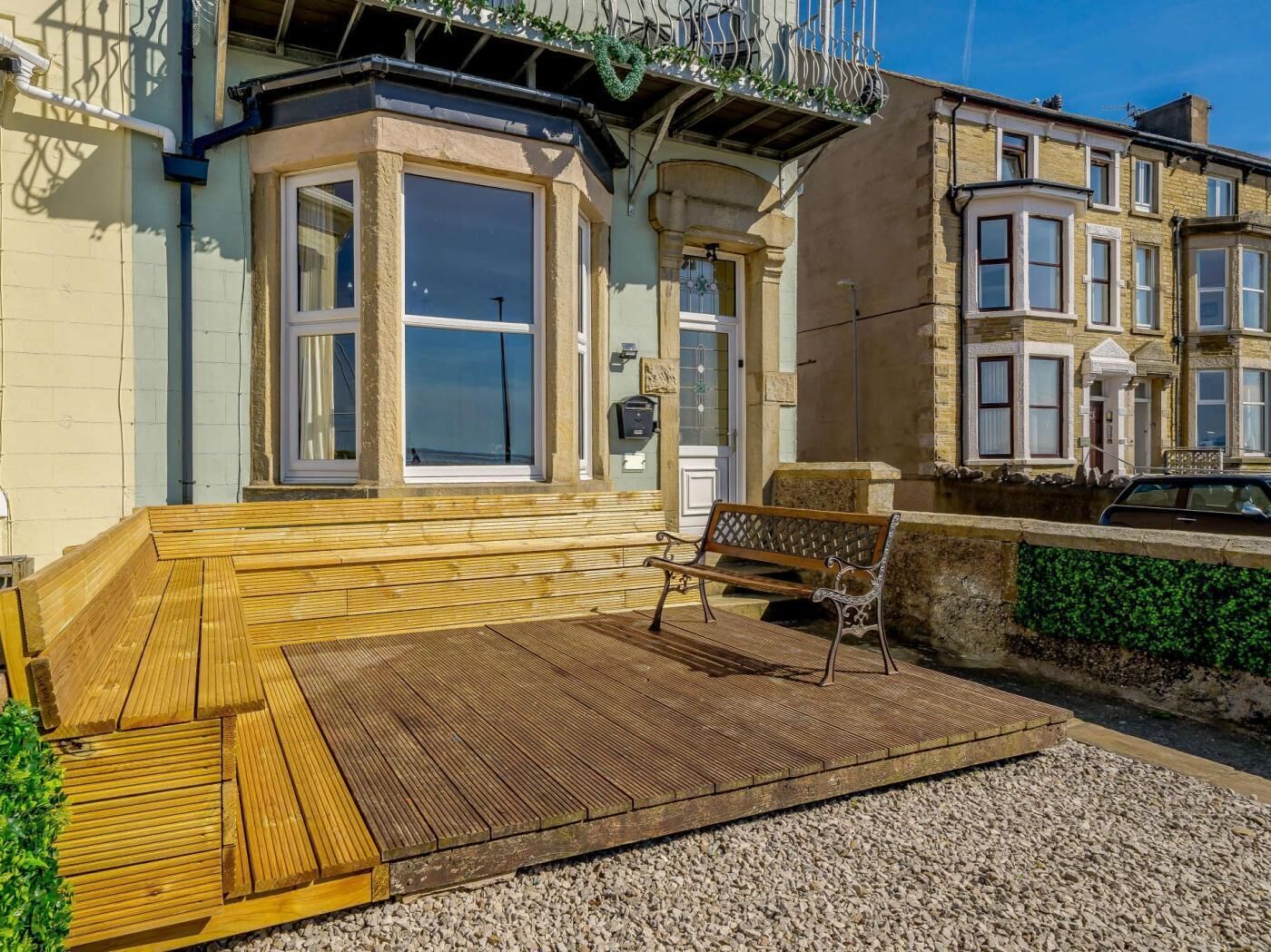 A corner building with a wooden deck, a bench, and a car parked nearby.