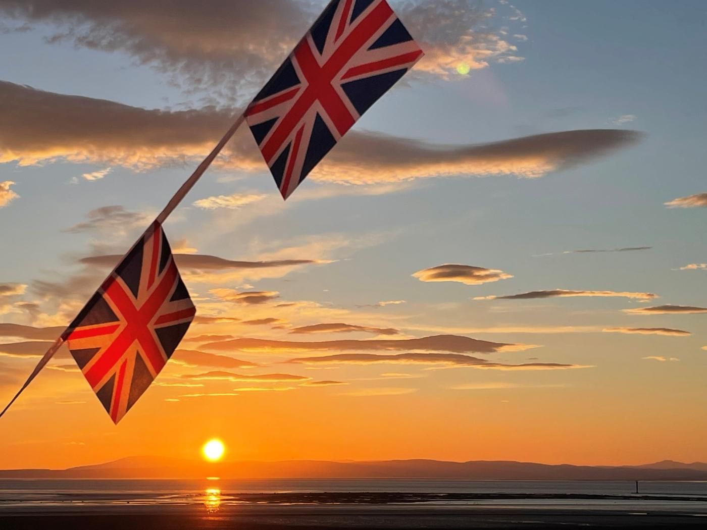 A sunset with two flags and a distant view of the sun.