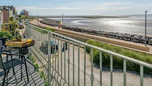 En balkong vid havet med utsikt över stranden, en matplats med utemöbler och en stenlagd gångväg.