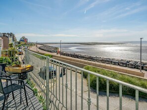 A seaside balcony with a view of the beach, a dining area with outdoor furniture, and a paved walkway. - 5 Bed in Morecambe (oc-87639) (Heysham)
