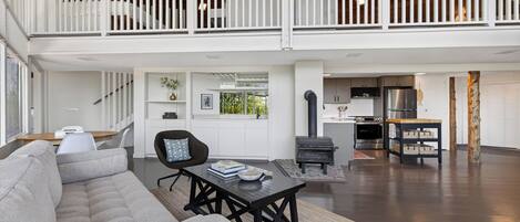 A spacious living area with a high ceiling, a fireplace, a kitchen with modern appliances, and a balcony with white railings.