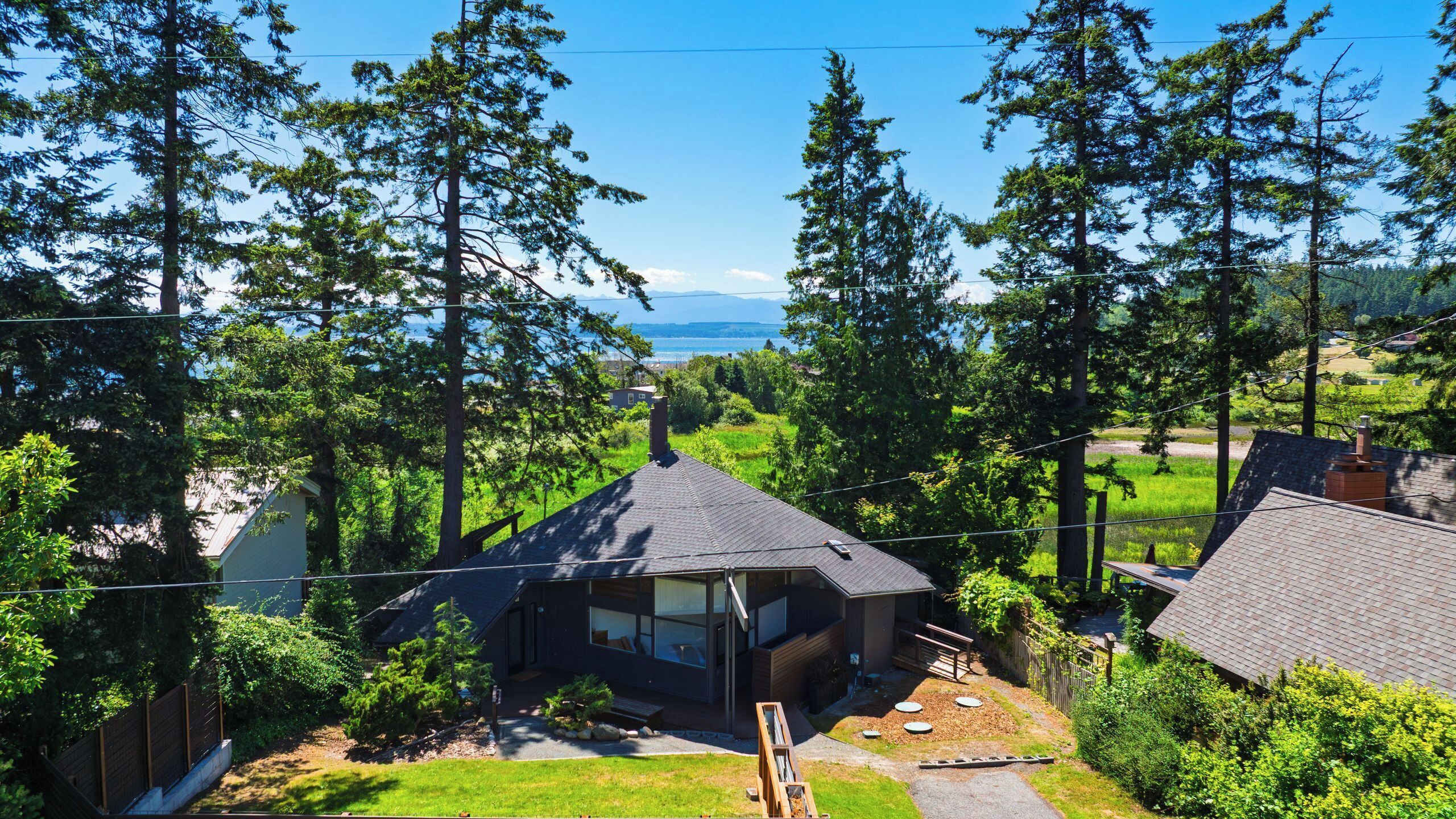 Une maison moderne dotée d’une grande baie vitrée, entourée d’arbres denses et offrant une vue sur la mer.