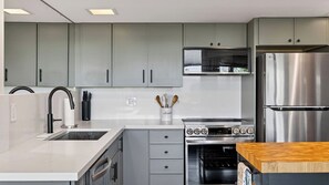 Una cucina moderna con mobili grigi, un frigorifero in acciaio inox, un forno integrato e un piano di lavoro con un tagliere in legno.