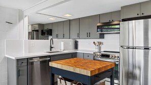 A modern kitchen with grey cabinets, a stainless steel refrigerator, a wooden table, and a built-in oven. - The Grove at Mutiny Bay by Avantstay Walk to Beach Shared Pool + Pickleball Court + Water Views (Freeland)