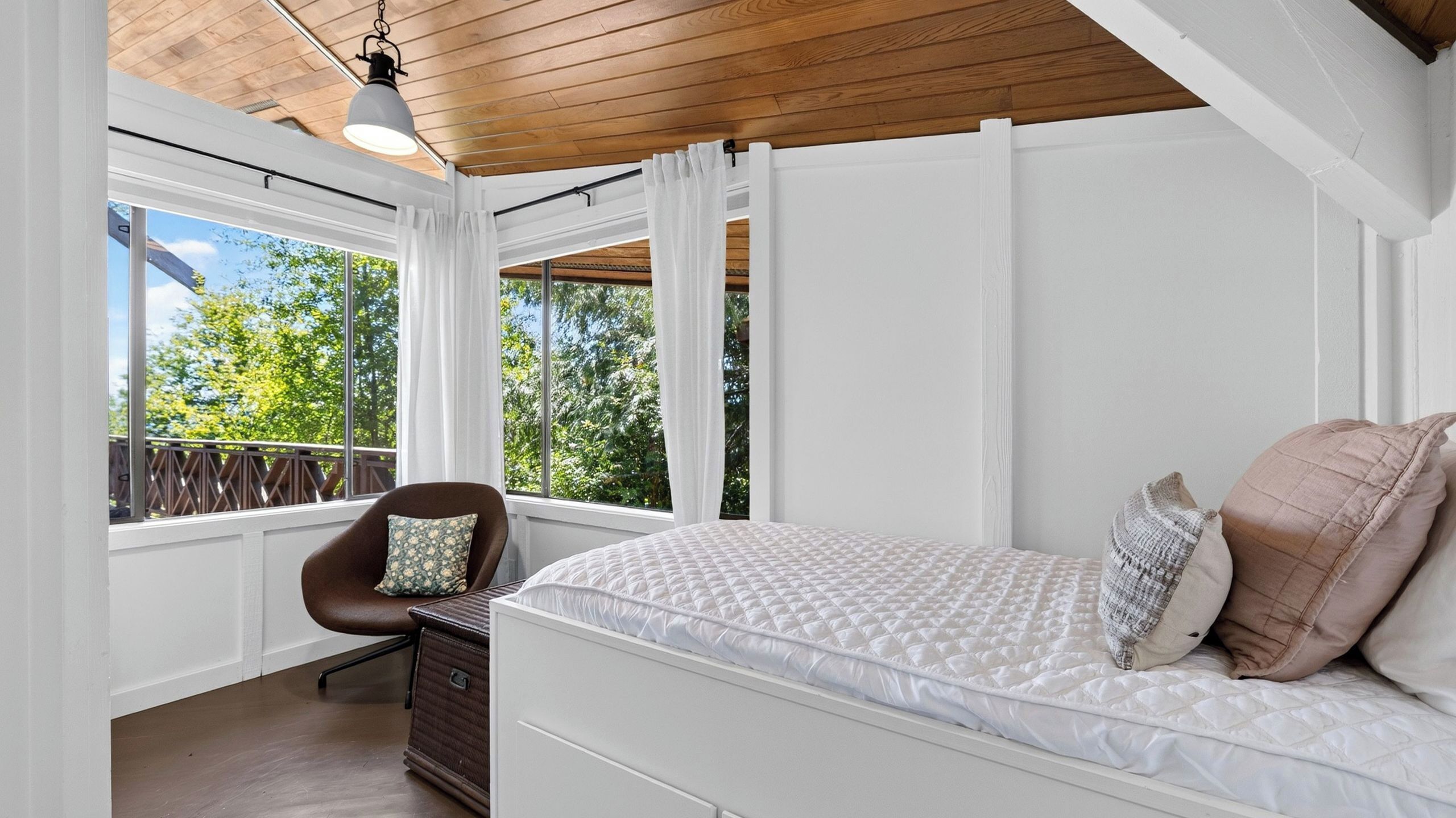 Une chambre à coucher avec un lit, une chaise, une commode et de grandes fenêtres.