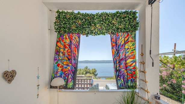 Ein Balkon mit Meerblick, eine hängende Pflanze, ein herzförmiger Schmuck und eine Lampe.