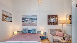 Ein Schlafzimmer mit einem Bett, einem Sessel, einem kleinen Tisch und Kunstwerken an den Wänden.