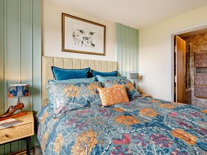 A bedroom with a floral-patterned bedspread, a headboard, a framed artwork, and a wooden nightstand with a lamp. - 1 Bed in Sherborne (oc-87292) (Lillington)