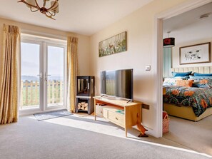 Um quarto com televisão, estante de livros, cama com roupa de cama colorida e um quadro na parede.