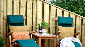 Zwei Holzstühle mit grünen Kissen, ein kleiner Holztisch und eine Champagnerflasche.