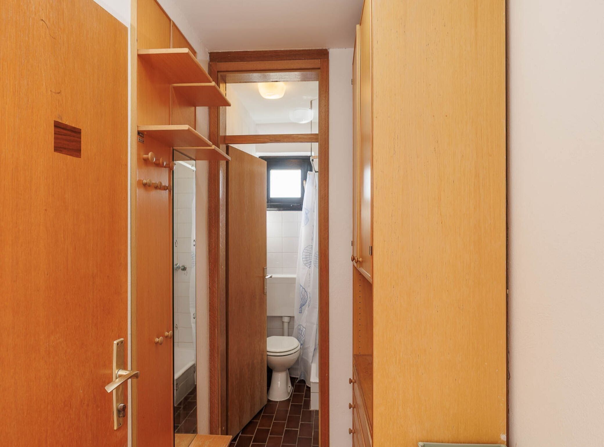 Een smalle gang met houten deuren en een zichtbare badkamer met toilet en douche.