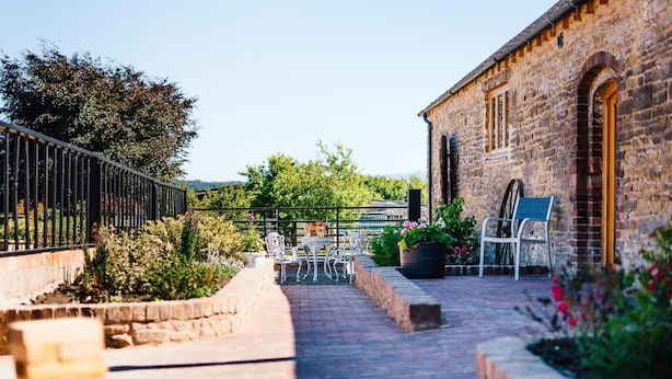 A courtyard with stone walls, a paved walkway, outdoor seating, and a brick building. - 4 Bed in Church Stretton (oc-87695) (Gretton)