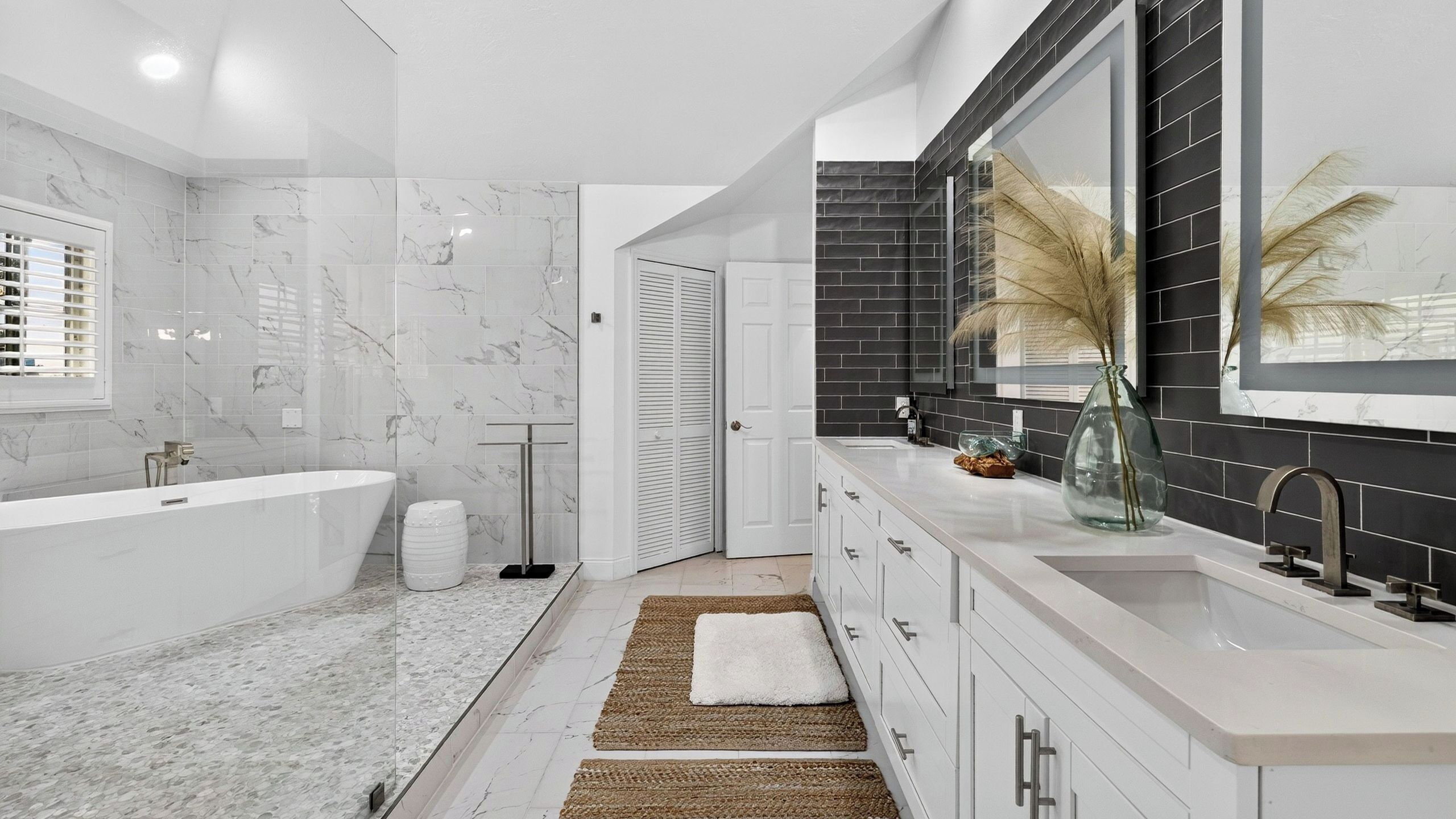 A modern bathroom with a freestanding bathtub, a large mirror, and a black tiled backsplash.