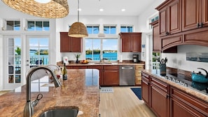 A modern kitchen with a large island, stainless steel appliances, and a view of the water. - Sunset Slip by Avantstay Private Pool + Dock + Bay Views Walk to Beach + Times Square (Fort Myers Beach)