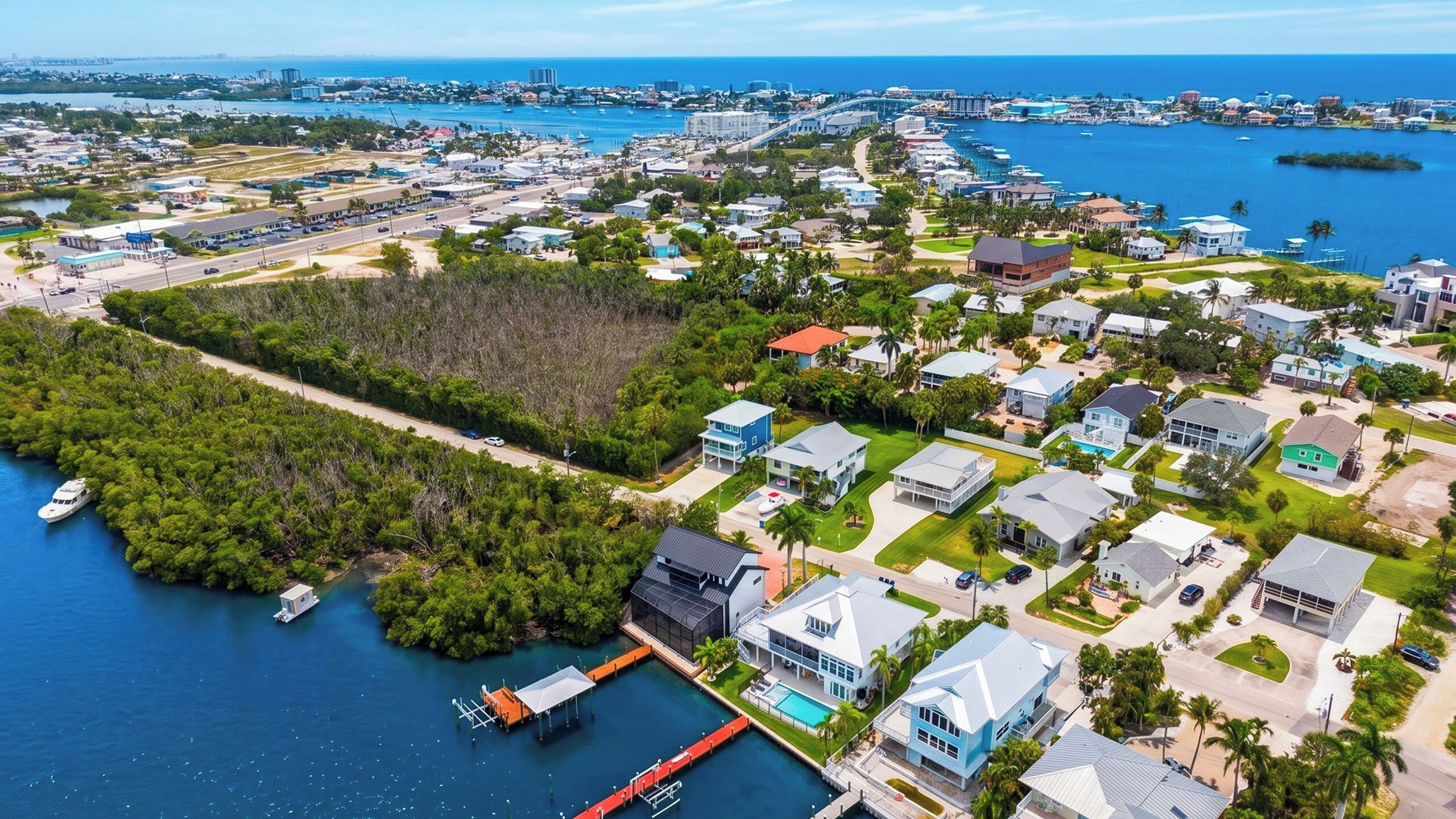 Vue aérienne d’une zone résidentielle côtière, avec des maisons, une marina et une vaste étendue d’eau.