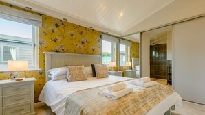 Quarto com uma cama, duas mesas de cabeceira com abajures, um encosto de cama e um espelho grande.