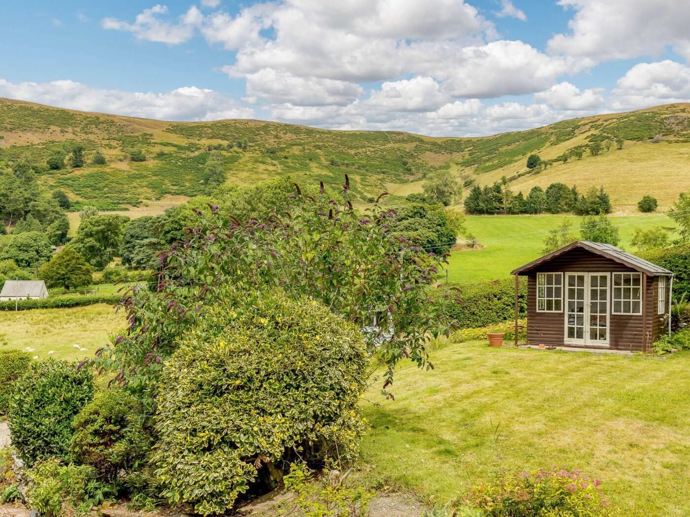 A rural landscape with rolling hills, a small wooden cabin, and a house in the background.