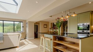 Een moderne keuken met een groot eiland, houten krukken en uitzicht op het buitengebied.