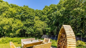 Mesa y bancos de madera al aire libre con paneles solares y una estructura para guardar leña.