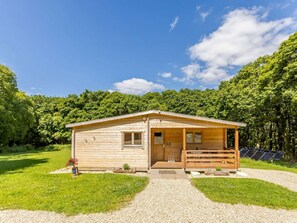 A wooden cabin with a porch, surrounded by a forest.