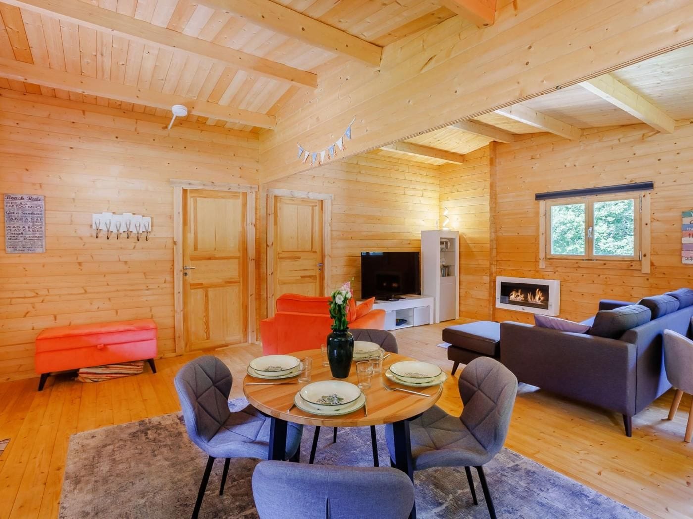 A wooden interior with a dining table, chairs, sofas, a television, and a fireplace.