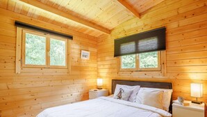 Un dormitorio de cabaña de madera con una cama, dos mesitas de noche, dos ventanas y un ventilador de techo.