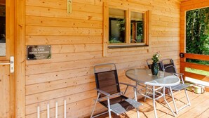 Una cabaña de madera con una mesa y sillas de vidrio, un termómetro y un letrero que solicita a los huéspedes quitarse los zapatos.