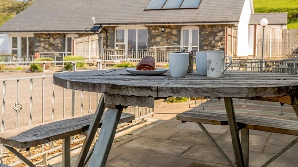 A stone house with a grey roof, a balcony, and a table with a plate, a teapot, and two cups. - 2 Bed in Bala (oc-87274) (Llandderfel)