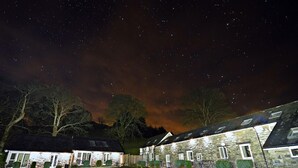 A stone building with multiple windows, a paved parking area, and a starry night sky. - 2 Bed in Bala (oc-87274) (Llandderfel)