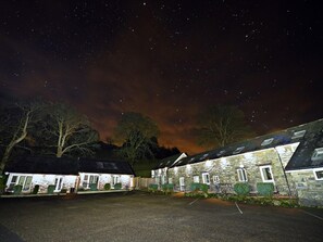 Un bâtiment en pierre doté de nombreuses fenêtres, une aire de stationnement pavée et un ciel nocturne étoilé.