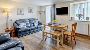 A modern living room with a leather sofa, a wooden dining table, and a TV mounted on the wall. - 2 Bed in Bala (oc-87274) (Llandderfel)