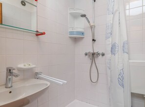 Et badeværelse med vask, spejl, brusebad og en hylde i glas.