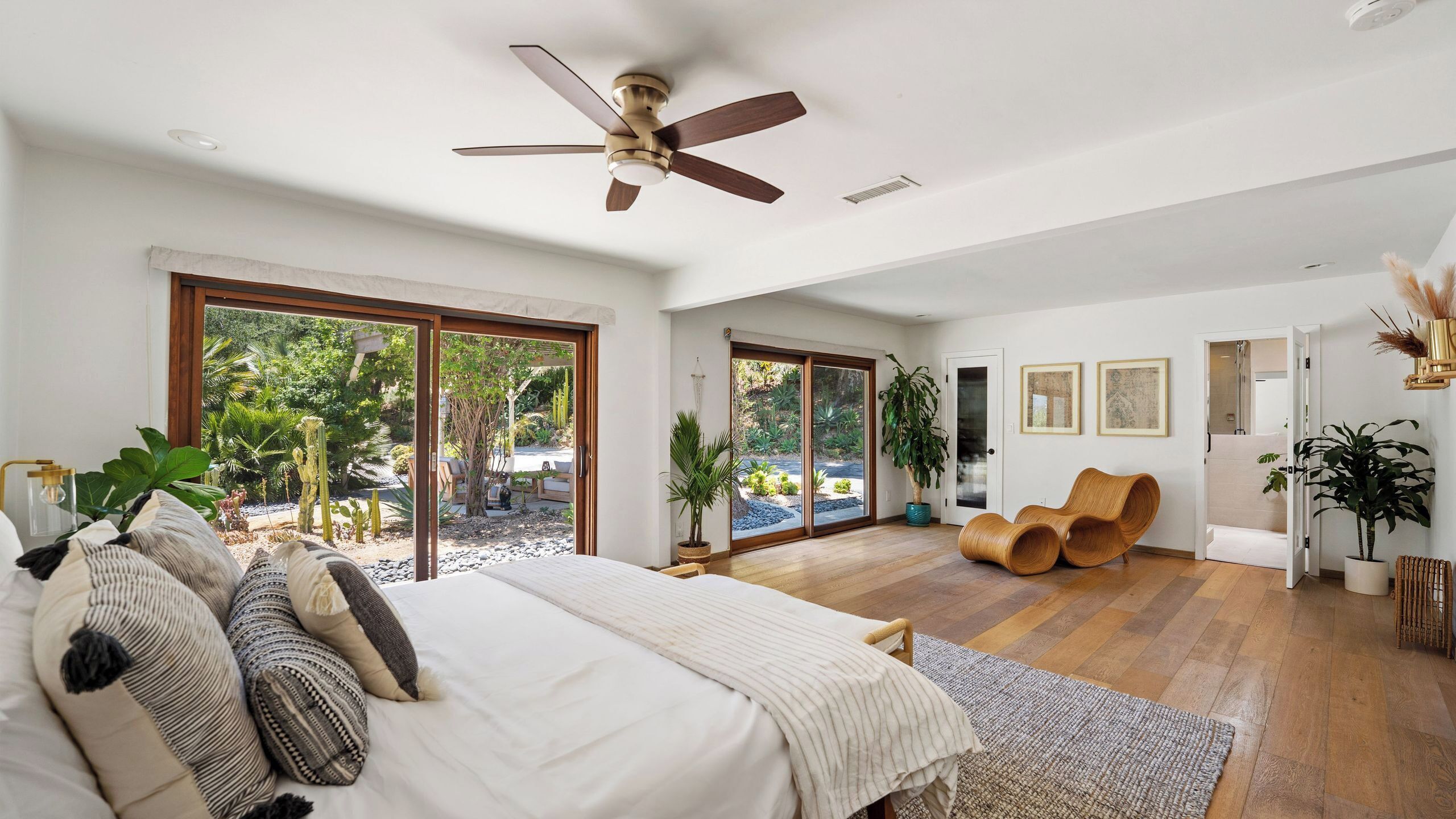 Une chambre spacieuse avec un grand lit, un ventilateur de plafond et une vue sur un jardin, accessible par des portes-fenêtres coulissantes.