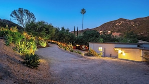 A gravel driveway leading to a building with a small attached garage, surrounded by landscaped gardens and a palm tree. - Dreamsawake by Avantstay Saltwater Pool Swim Spa + Firepit Private Canyon Views (Calabasas)