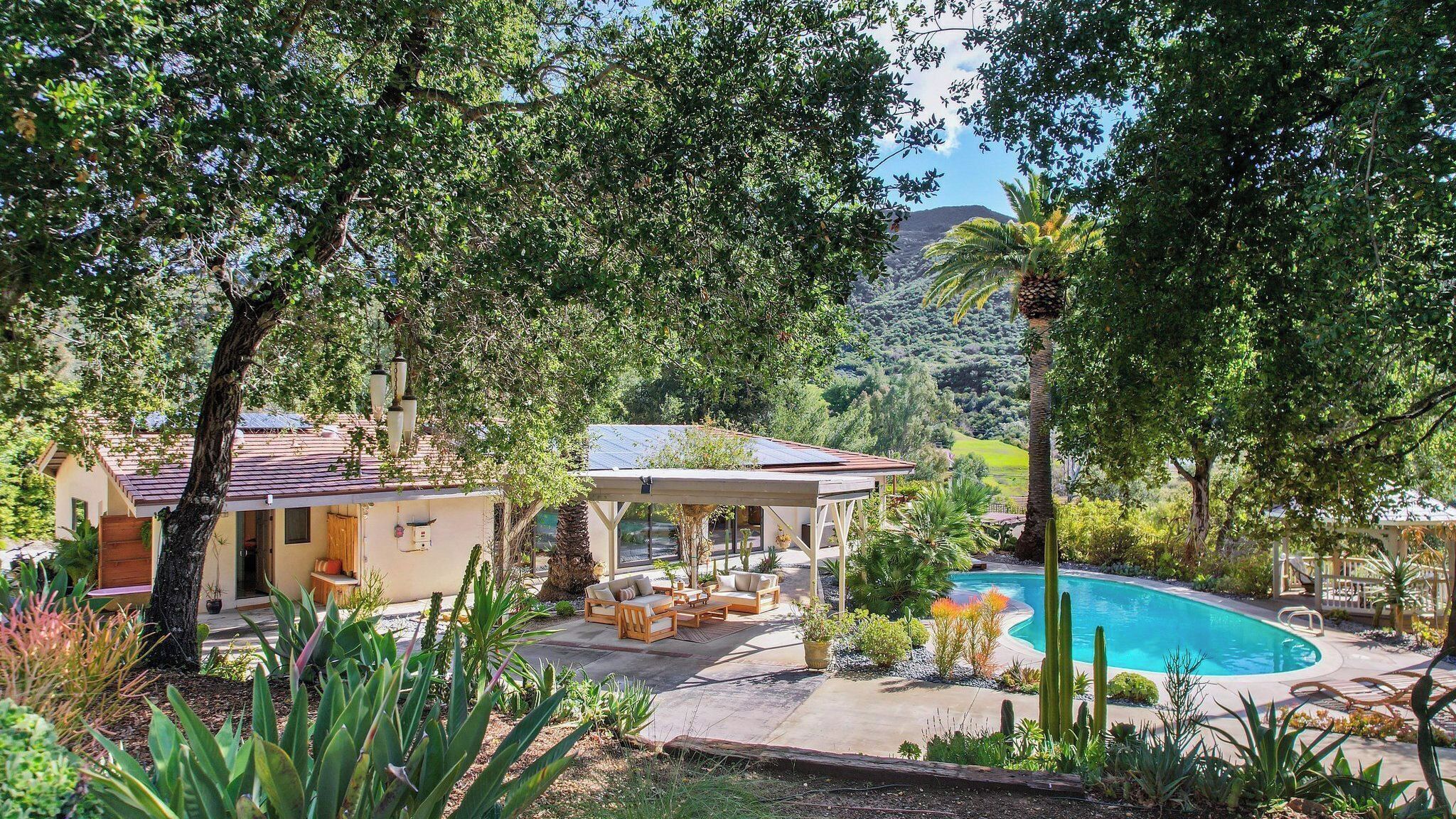 Uma casa com piscina, rodeada por árvores e uma montanha ao fundo.