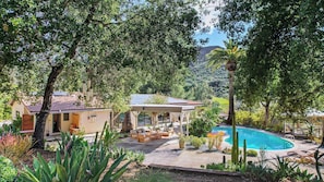 Uma casa com piscina, rodeada por árvores e uma montanha ao fundo.
