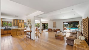 A spacious living area with a wooden floor, a dining table, sofas, and a large window overlooking a pool. - Dreamsawake by Avantstay Saltwater Pool Swim Spa + Firepit Private Canyon Views (Calabasas)