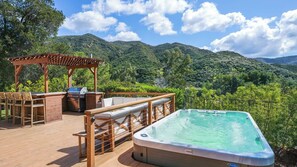 A wooden deck with a hot tub, outdoor seating, and a barbecue area overlooking a mountainous landscape. - Dreamsawake by Avantstay Saltwater Pool Swim Spa + Firepit Private Canyon Views (Calabasas)