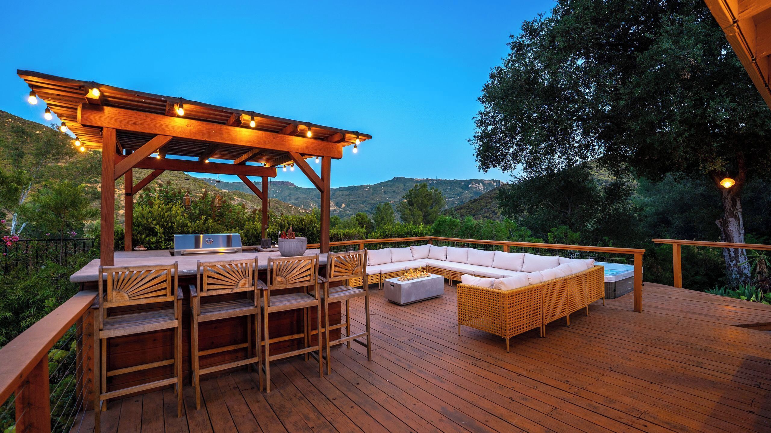 A wooden deck with outdoor furniture, a grill, and a pergola with lights.