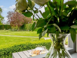 A garden view with a table set for a meal, a vase with flowers, and a hedge in the background. - 1 Bed in York (oc-87323) (Tockwith)