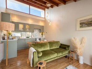 A modern kitchen with marble countertops, a green velvet sofa, wooden flooring, and a dining area with a small round table.
