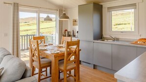 Un coin repas avec une table et des chaises en bois, une cuisine avec une fenêtre et une vue sur la campagne.
