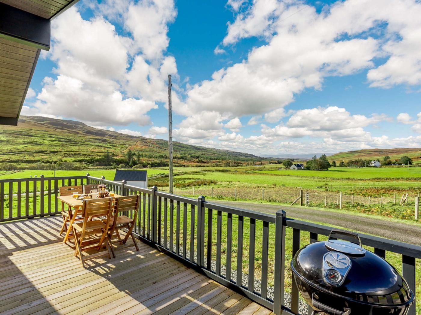 Une terrasse en bois avec une table et des chaises, donnant sur un paysage rural composé de champs et de maisons.